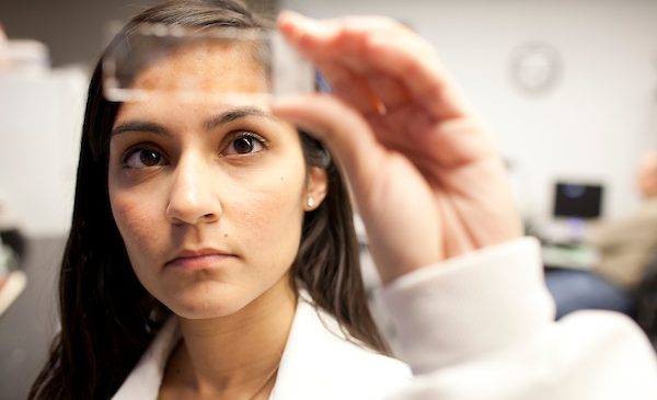 female student wearing a white coat looking at a slide in the light