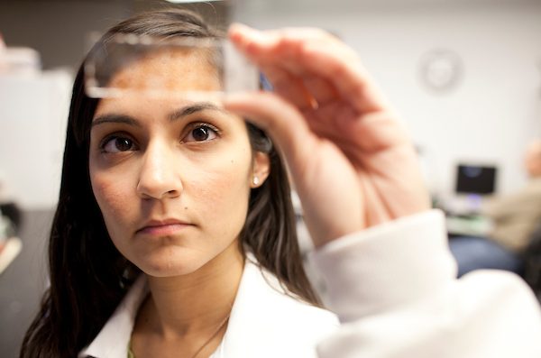 Female student in a white lab coat looking at a slide