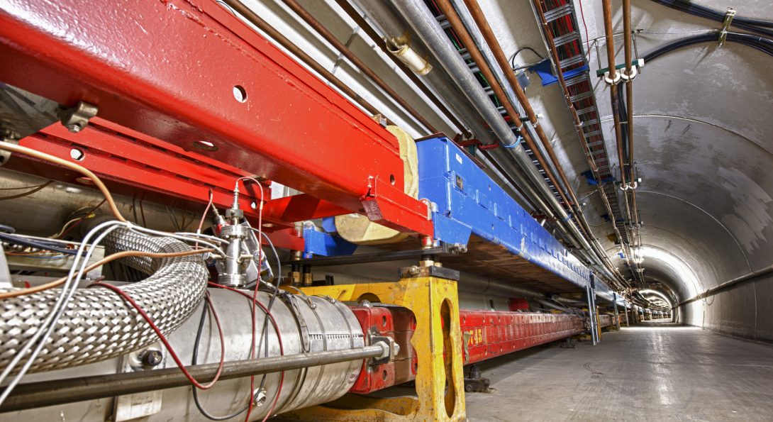 A long concrete tunnel with large blue and red scientific equipment on one side.