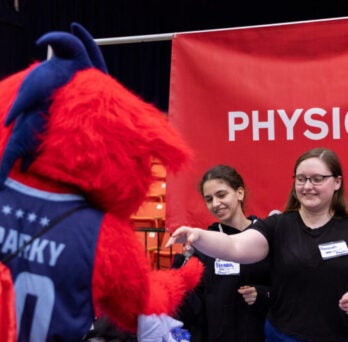 Two UIC Physics undergraduates interacting with UIC mascot Sparky at UIC Ignite event 